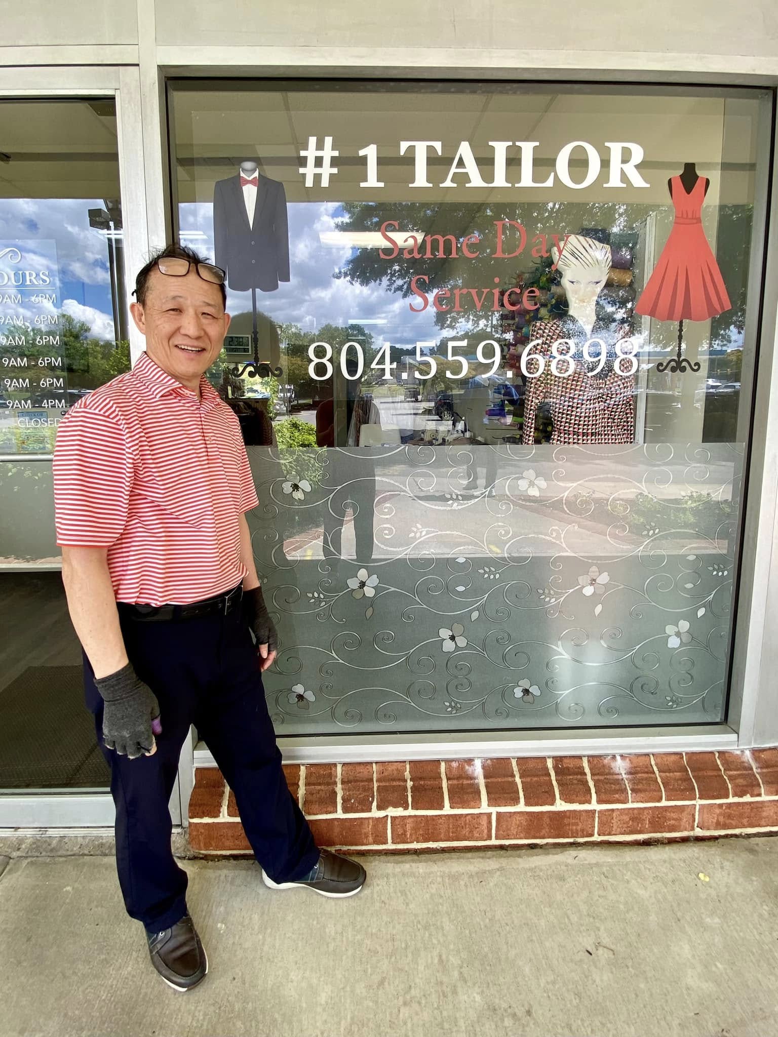 A smiling man outside the #1 Tailor shop beside its original window sign